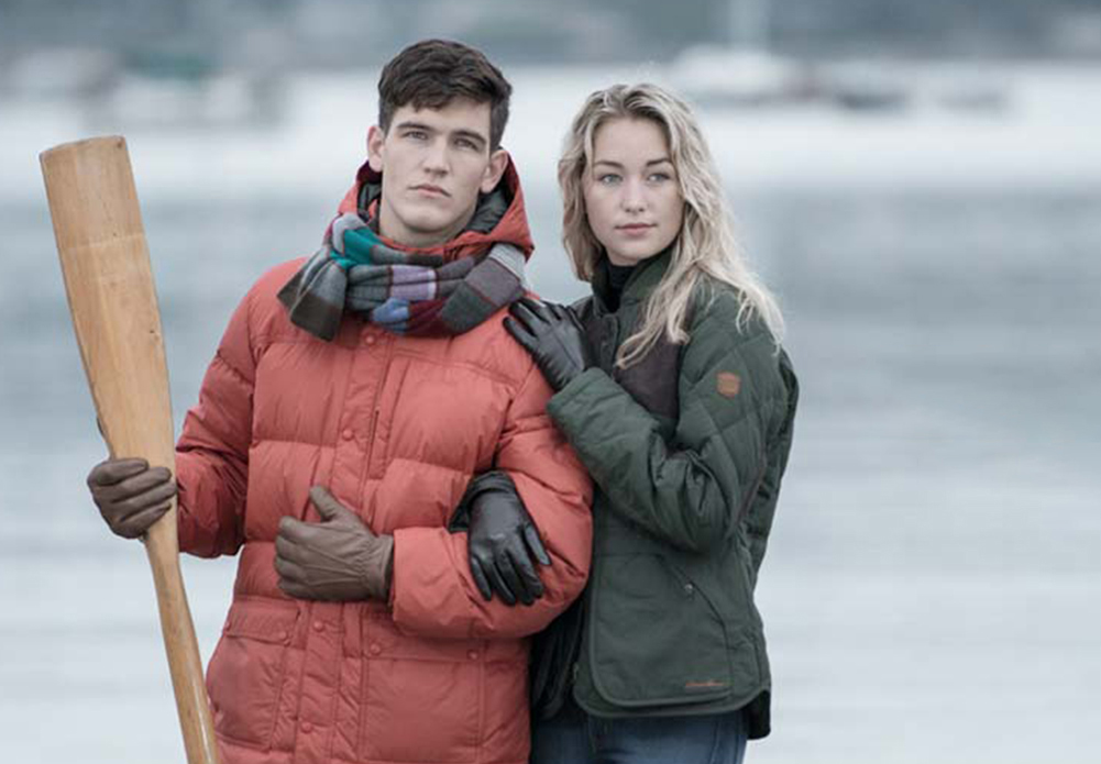 A snowy lake with man holding an ore and a woman beside him, her arm around his, both wearing Pratt and Hart gloves.